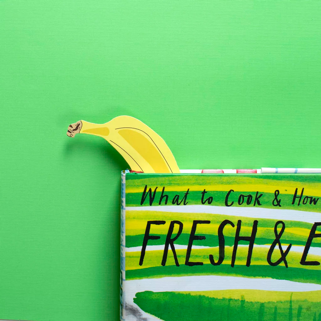 Yellow banana peeking out from a cookbook titled 'What to Cook & How' on a green background