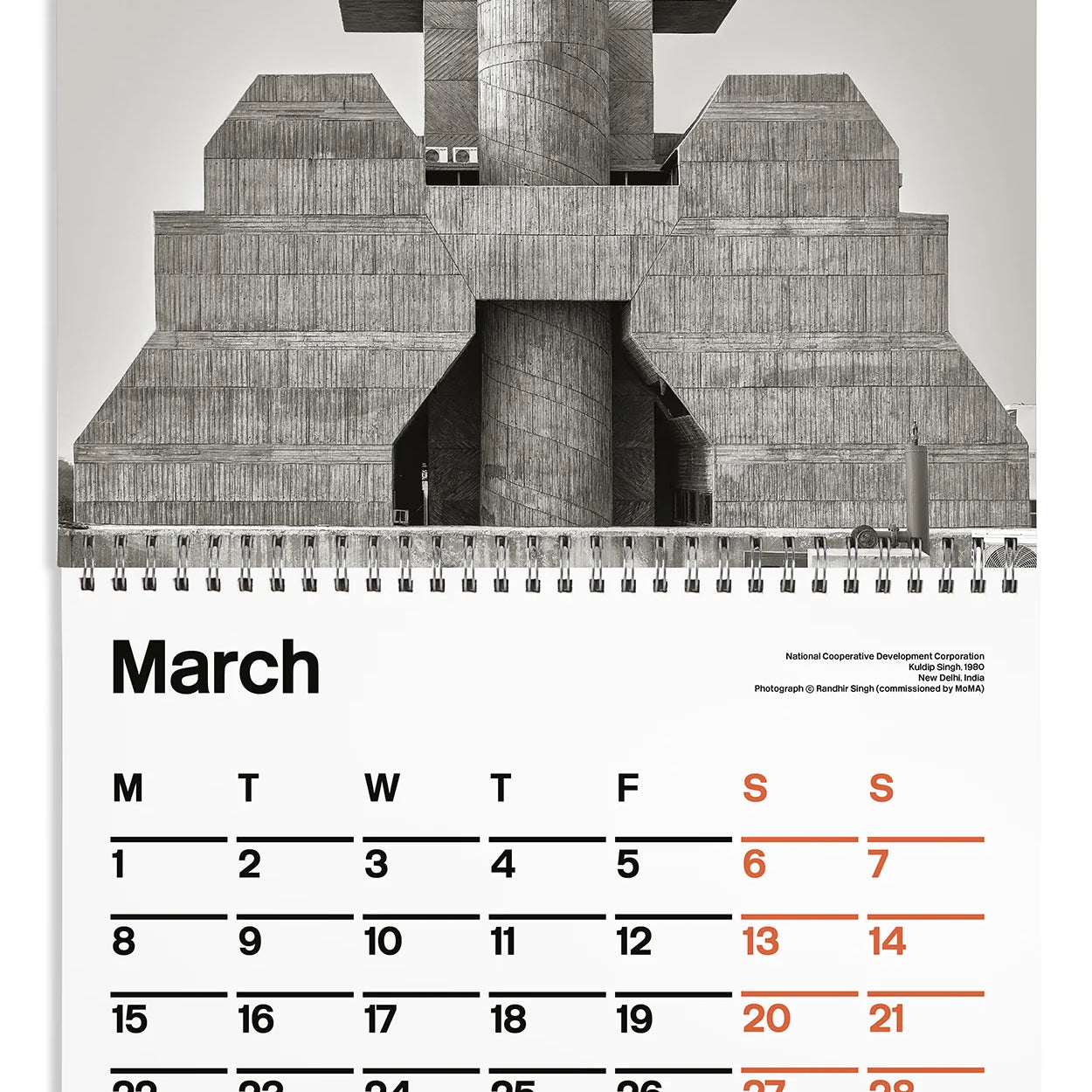 A spiral-bound calendar page featuring a large black-and-white architectural photograph of a concrete building on the top half, with a March calendar grid on the bottom half. The days of the week are printed in black, with Sundays highlighted in red-orange.