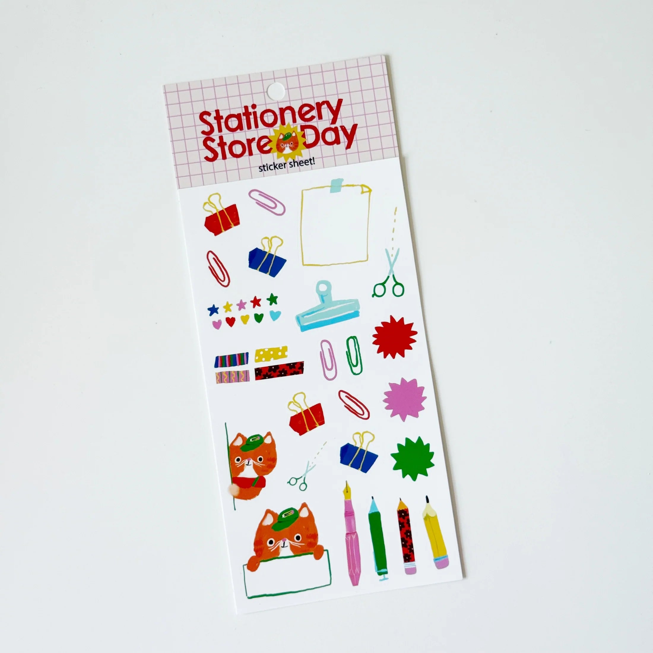 A sheet of colorful stationery stickers on a white backing card, photographed on a plain white background. The header reads 'Stationery Store Day' and the stickers include paperclips, scissors, stars, hearts, pencils, and cartoon foxes.