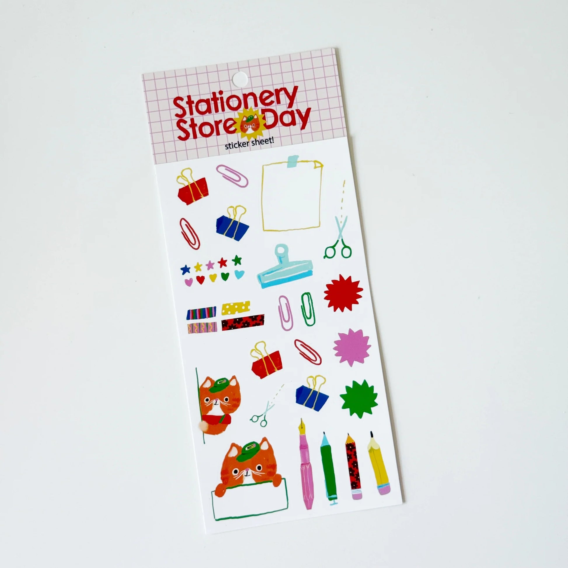 A sheet of colorful stationery stickers on a white backing card, photographed on a plain white background. The header reads 'Stationery Store Day' and the stickers include paperclips, scissors, stars, hearts, pencils, and cartoon foxes.