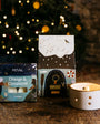 Decorative candles and packaging with a Christmas tree in the background