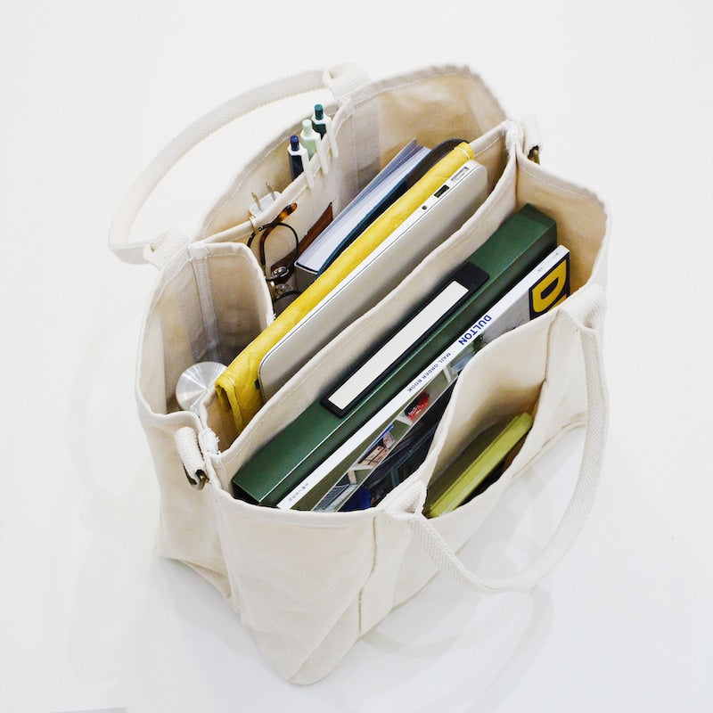 Beige tote bag with compartments filled with books and office supplies on a white background