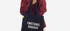 Person holding a black tote bag with 'EMOTIONAL BAGGAGE' text on a white background