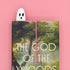 Book titled 'The God of the Woods' with a ghostly figure on a pink background