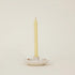 White ceramic candle holder with a single beige candle on a light beige background