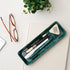 Green tray with stationery items on a desk with glasses and a plant.