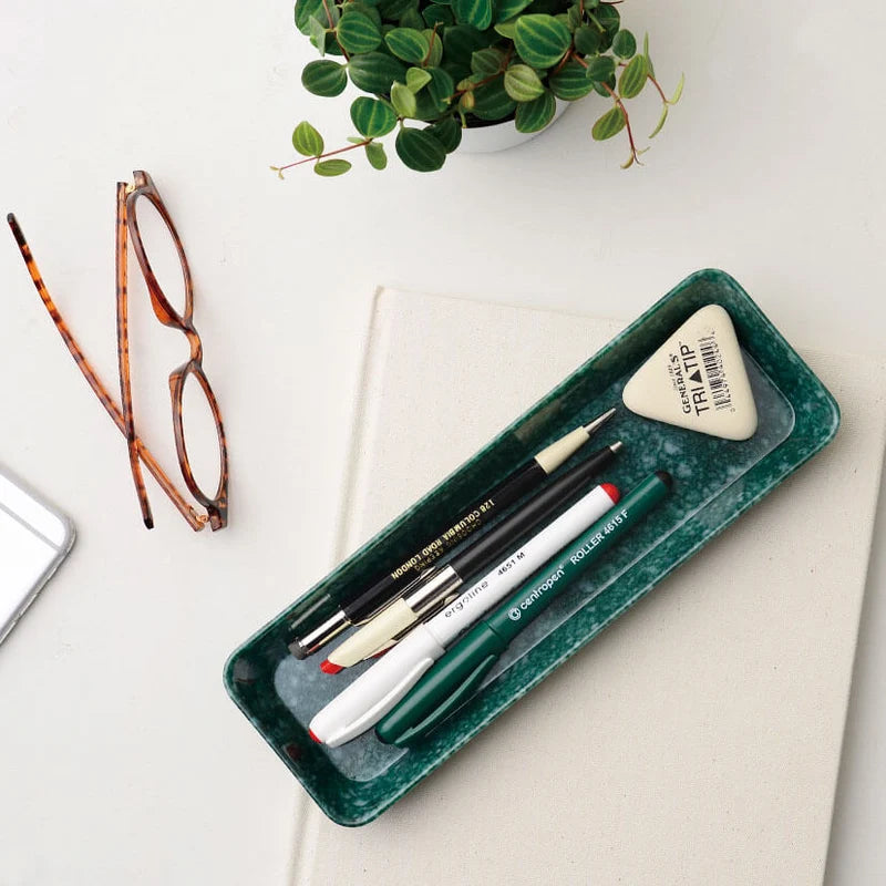 Green tray with stationery items on a desk with glasses and a plant.
