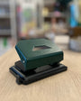 Green and black hole puncher on a wooden surface with a blurred background