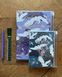 Two notebooks with crane designs on a wooden surface with a pen and ruler.