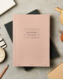 Pink notebook with 'Notebook' text on a gray surface with stationery items.