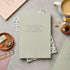 Green notebook on a gray surface with office supplies and a cup of coffee.