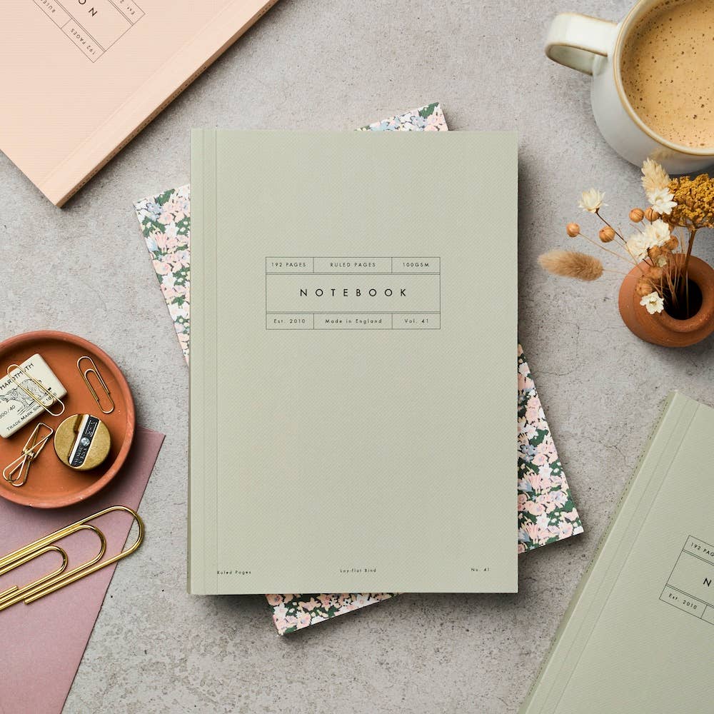 Green notebook on a gray surface with office supplies and a cup of coffee.
