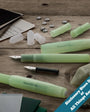 Green fountain pens and ink cartridges on a wooden surface with stationery items.