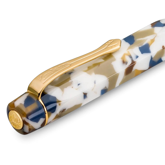 A close-up of a fountain pen with a marbled resin body in white, gold, and navy blue, featuring a polished gold clip and end cap.