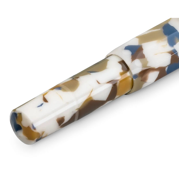 A close-up of a pen barrel with a marbled resin pattern in white, brown, tan, and blue on a clean white background.