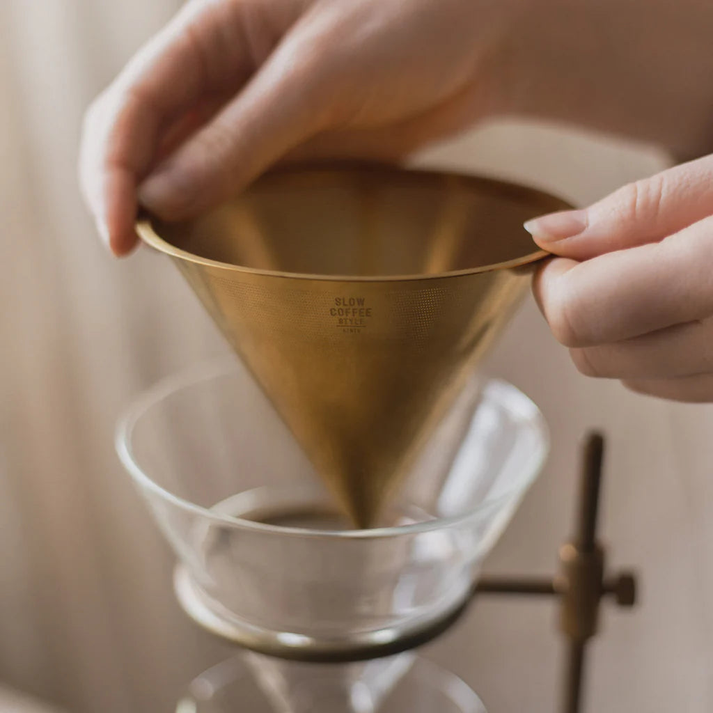 Person holding a gold coffee filter over a glass container