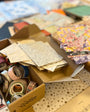 Box containing stationery items including paper, envelopes, and tape on a table.