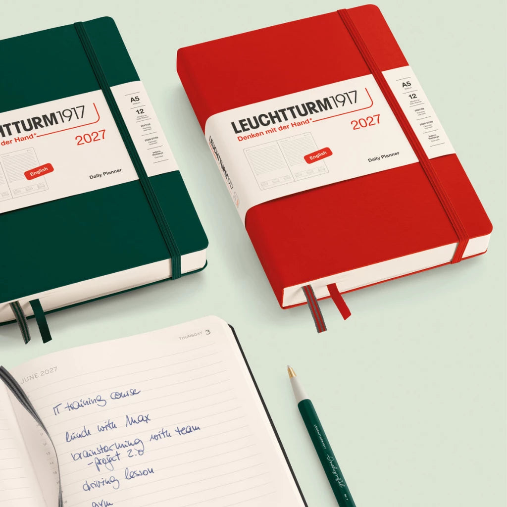 Two Leuchtturm1917 notebooks, one green and one red, on a light green background with a pen.
