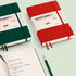 Two Leuchtturm1917 notebooks, one green and one red, on a light green background with a pen.