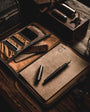 Brown leather travel set with stationery items on a wooden surface