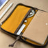 A pocket journal with a waxed canvas cover, displayed alongside a pen and cables, revealing the interior dot grid refill and organization pockets.