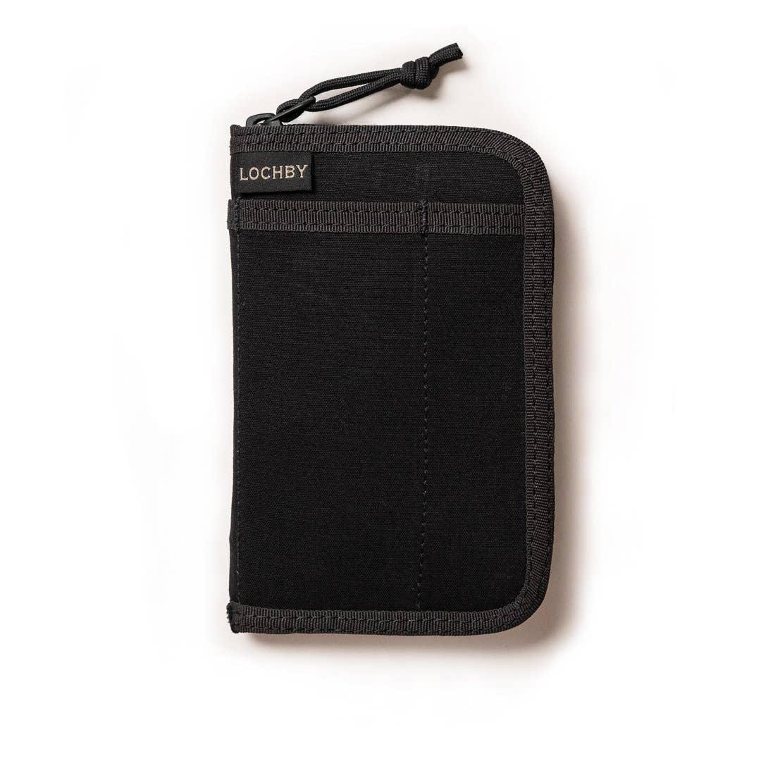 A pocket journal with a waxed canvas cover, displayed alongside a pen and cables, revealing the interior dot grid refill and organization pockets.