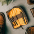 A brown and yellow venture pouch with elastic loops and pockets, alongside a pair of shoes and a bag, suggesting it can be carried in a bag or used as a crossbody bag.