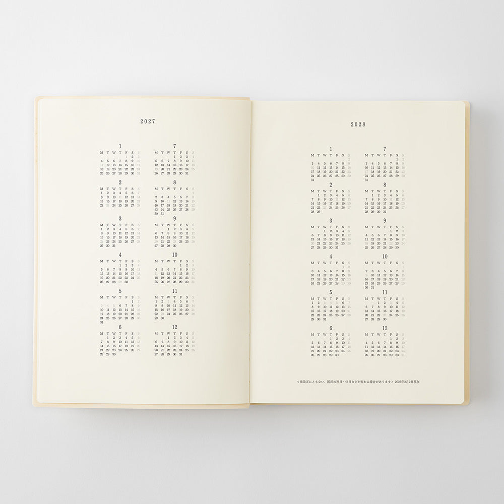 An open book or journal showing two cream-colored pages with printed calendar grids for 2017 and 2018 in gray text, photographed against a light gray background.