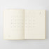 An open cream-colored planner or journal showing a minimalist monthly calendar layout on both pages, photographed from above on a light gray background.