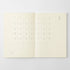 An open cream-colored planner or calendar showing minimalist monthly grids and dates on both pages, photographed against a light gray background.
