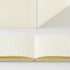 A cream-colored grid notebook shown both closed and open, with the open view displaying double-column lined pages and the closed view showing the cover and spine.