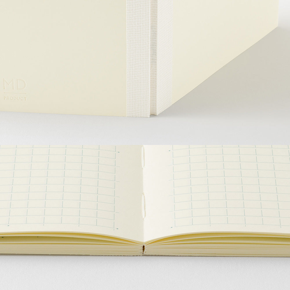 A cream-colored grid notebook shown both closed and open, with the open view displaying double-column lined pages and the closed view showing the cover and spine.