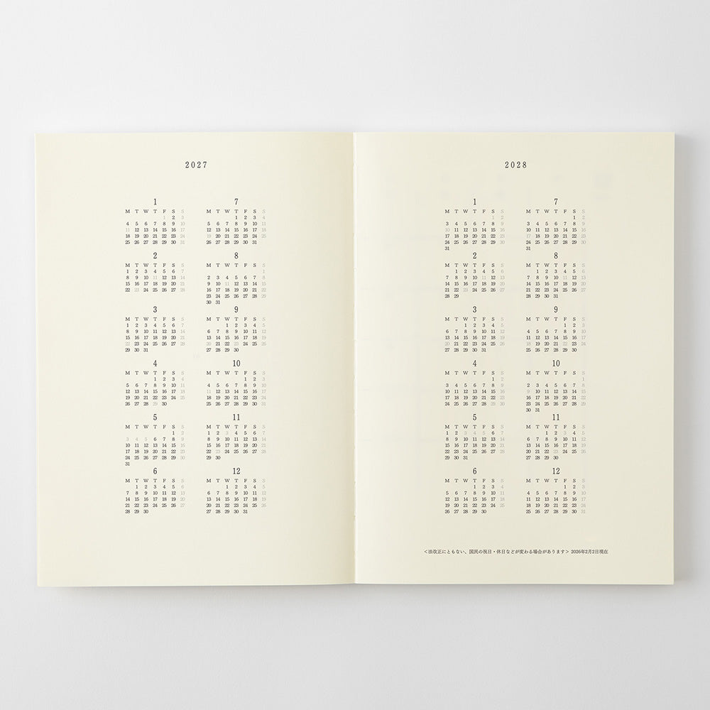 An open book or planner spread showing calendar pages for 2027 and 2028, with small monthly grids printed in gray on warm off-white pages, photographed against a light gray background.