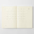 An open cream-colored planner or journal showing a minimalist monthly calendar layout on both pages, photographed against a light gray background.