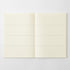 An open notebook with blank, lined cream-colored pages, displayed flat against a light gray background.
