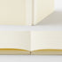 A cream-colored lined notebook shown both closed and open, highlighting the lined pages and spine texture against a clean white background.
