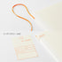 A cream-colored hardcover diary with an orange elastic loop handle, shown alongside a matching cream index sticker sheet with orange printed text. The image is set against a clean white background with Japanese text indicating an index sticker is included.