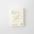 An A7 size monthly planning notebook by MD Product, featuring a minimalist cream cover with black line art of a hand writing and Japanese text.