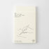 A cream-colored monthly planner cover with minimalist black line art of a hand writing, shown on a light gray background.