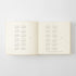 An open cream-colored book or journal showing printed calendar grids on both pages, photographed against a light gray background.