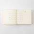 An open cream-colored planner or journal showing a minimalist monthly calendar grid on the left page and the date '1 Jan' on the right page, photographed against a light gray background.
