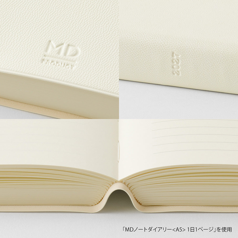 Cream-colored textured notebook cover and matching lined paper pages, shown in a close-up collage with embossed 'MD' branding and the year '2027'.