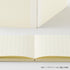 An open cream-colored grid notebook showing its double-page spread, with a matching closed notebook standing behind it on a white surface. Japanese text appears at the bottom right.
