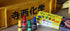 Four small bottles with colorful caps and a box on a wooden surface with a yellow sign in the background.