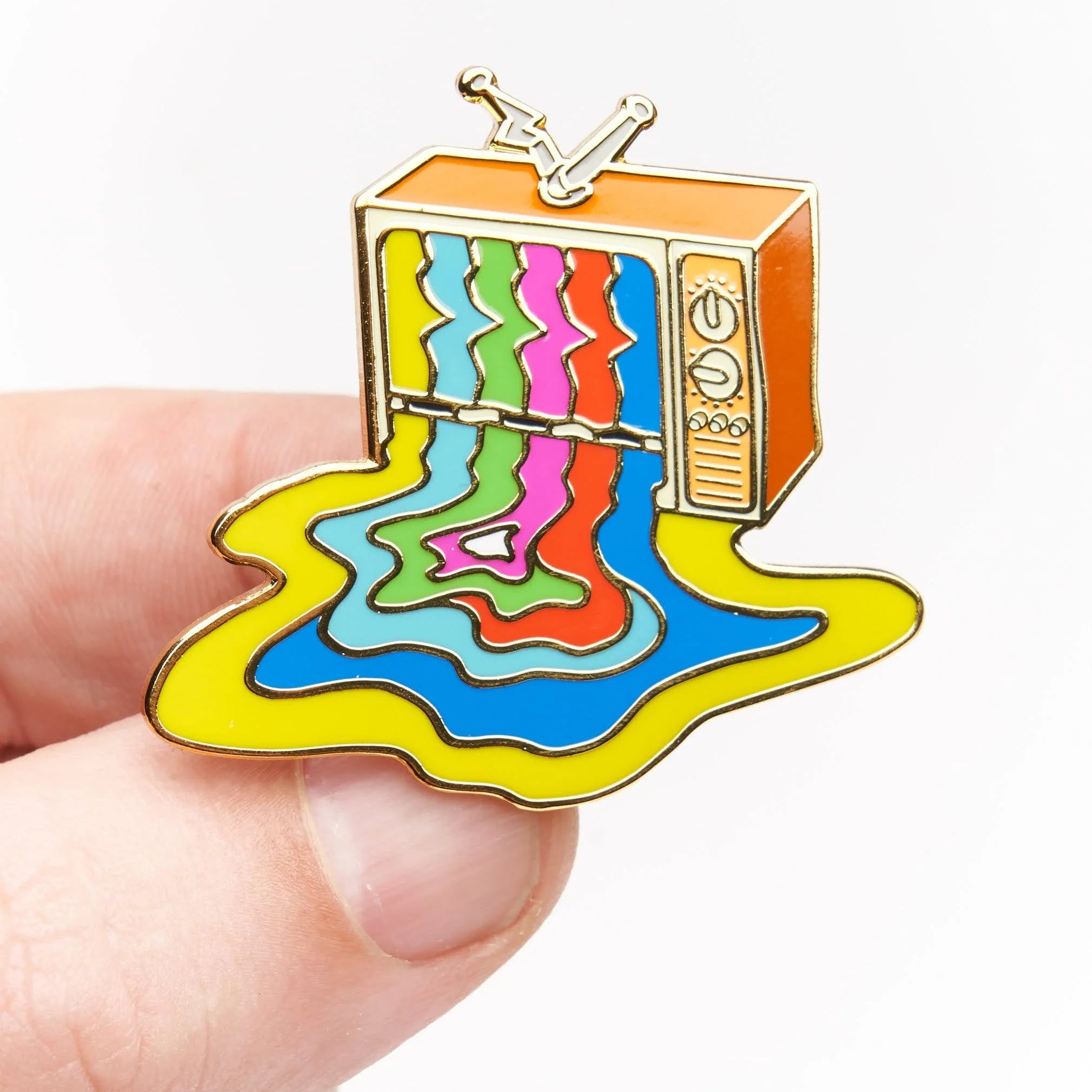 A small enamel pin shaped like a retro television with colorful dripping liquid patterns, held between fingers against a plain white background.