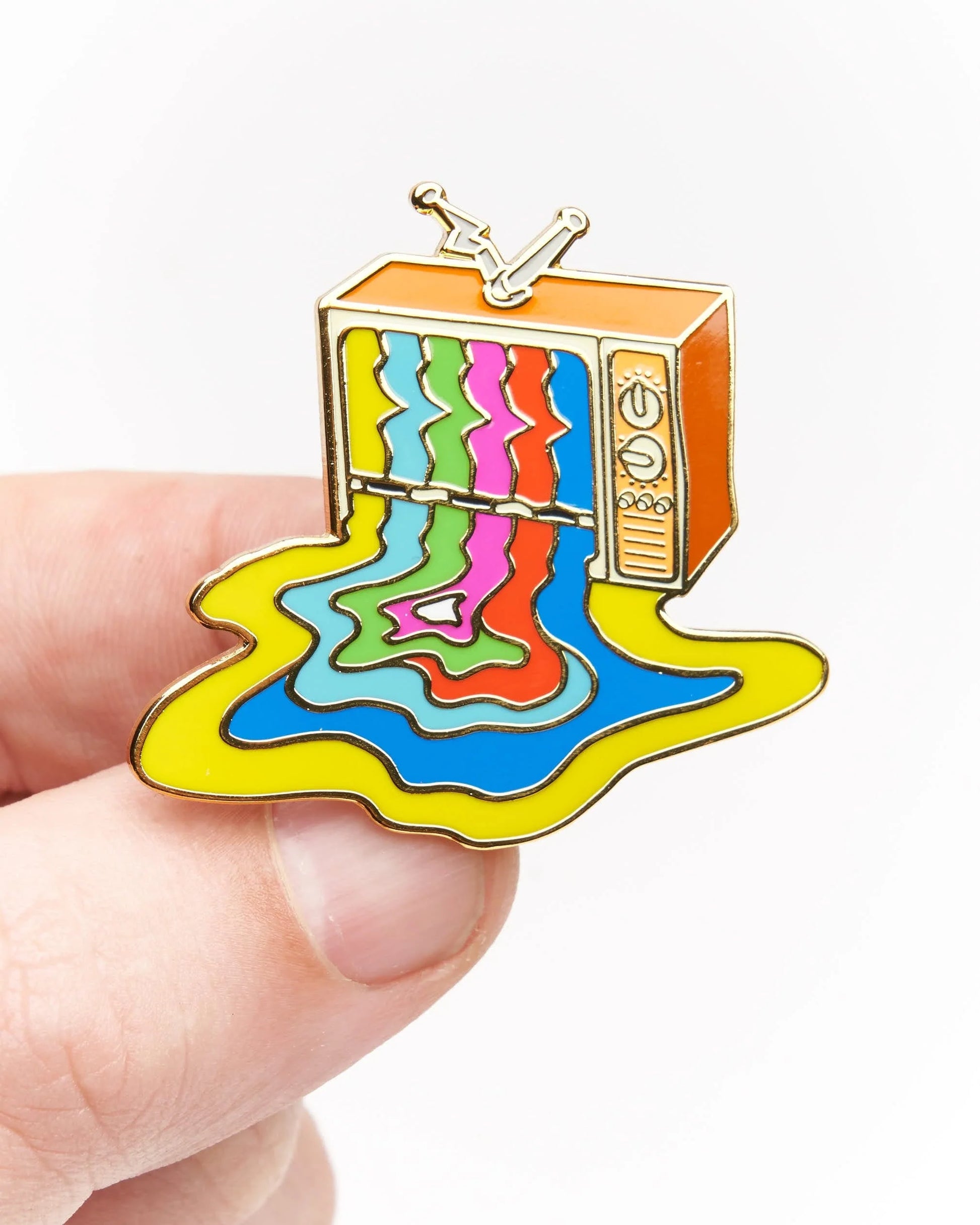 A small enamel pin shaped like a retro television with colorful dripping liquid patterns, held between fingers against a plain white background.
