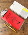 Red clipboard with a yellow pen on a wooden surface