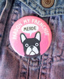 Pink button with a dog illustration and text on a denim background