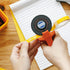 Person using a Benq tape measure on a wooden surface with a notebook in the background
