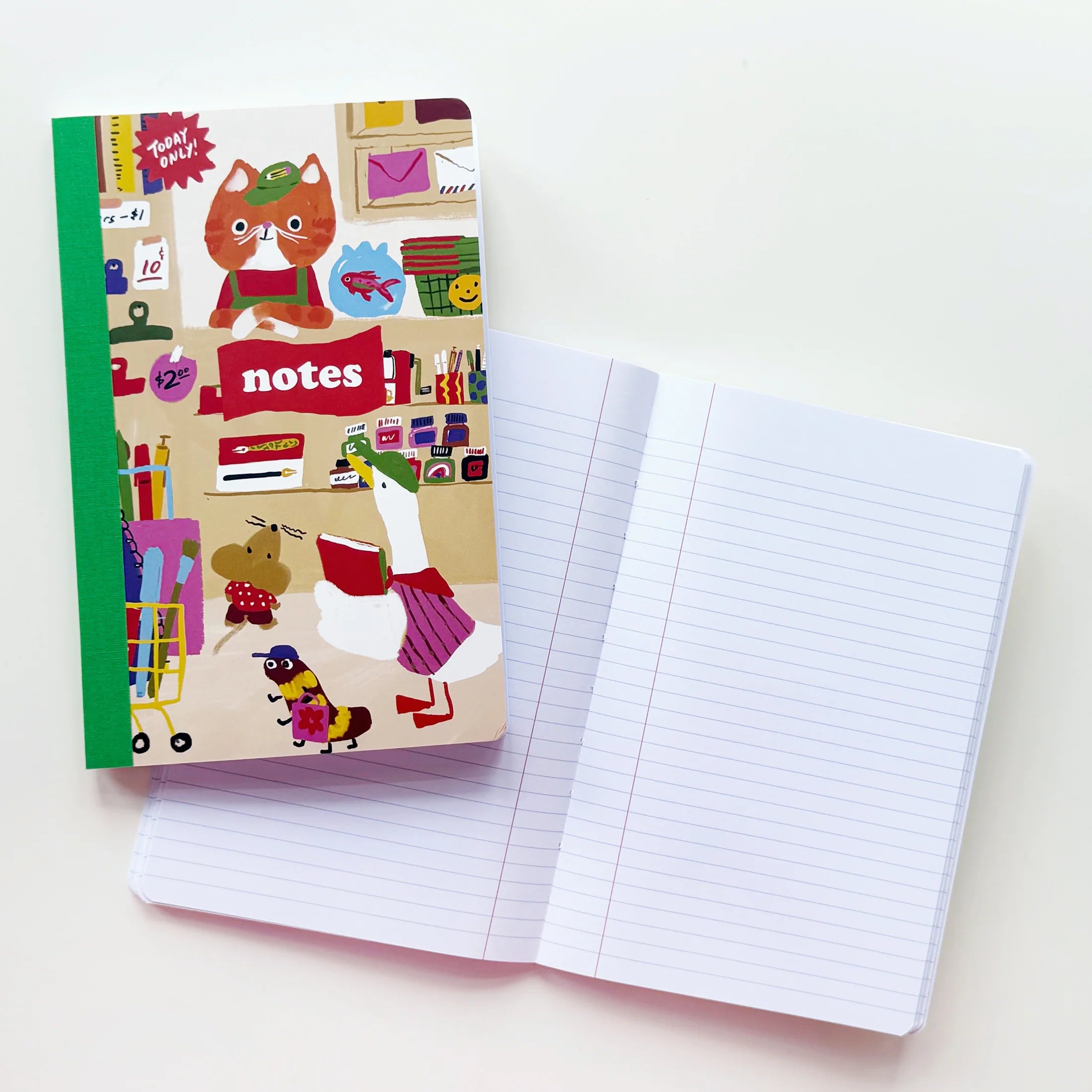 A lined notebook with a colorful illustrated cover featuring a cat in a shop, shown next to an open blank lined notebook on a clean white background.